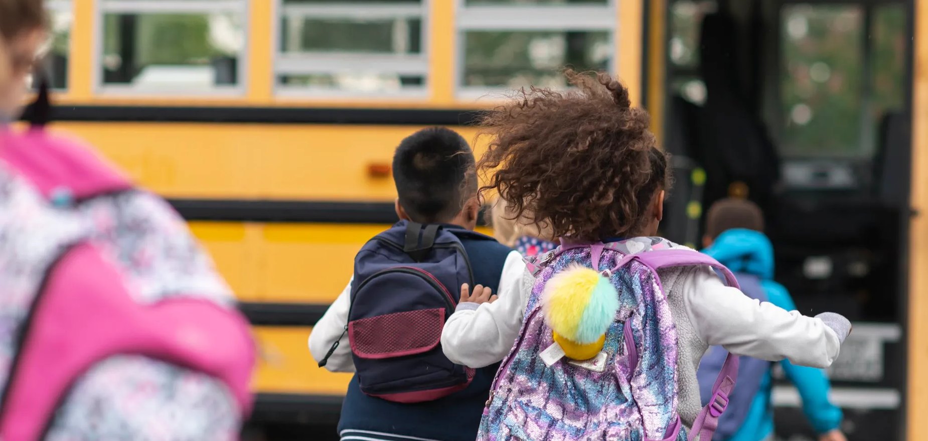 Students with backpacks heading to a school bus, for the Learning Can’t Wait education podcast.
