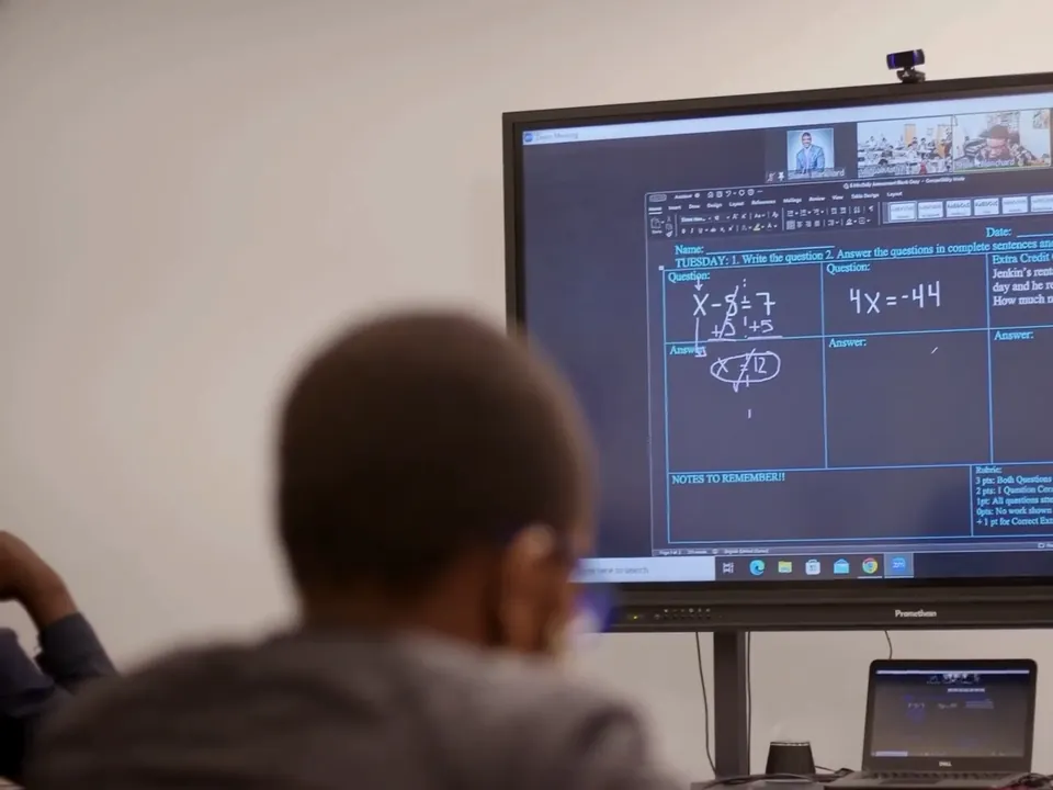 A student follows a live tutor's math lesson on the classroom display