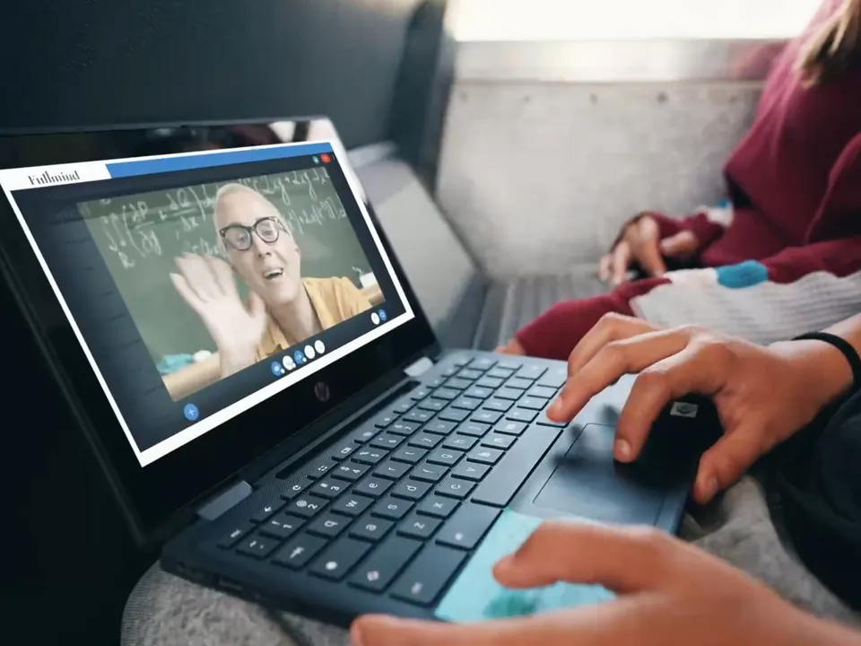 A student joins a live lesson on a laptop as the certified Fullmind teacher on screen waves, learning wherever they are staying